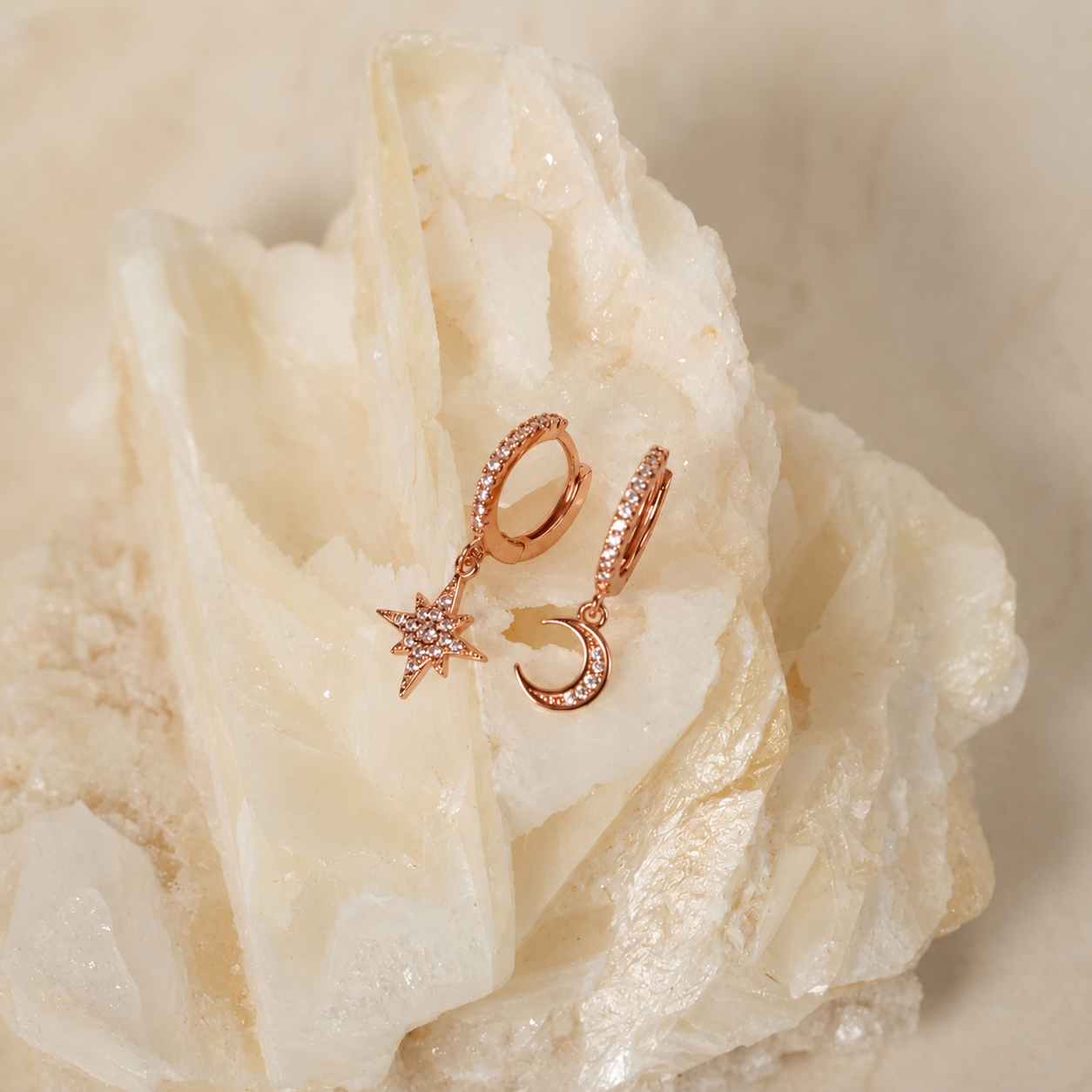 Rose gold crescent moon and star huggie hoop earrings with small clear crystal accents, displayed on a white crystal cluster.